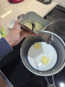 Measuring half a hollandaise sauce packet with a spoon, with milk and butter sitting in a saucepan