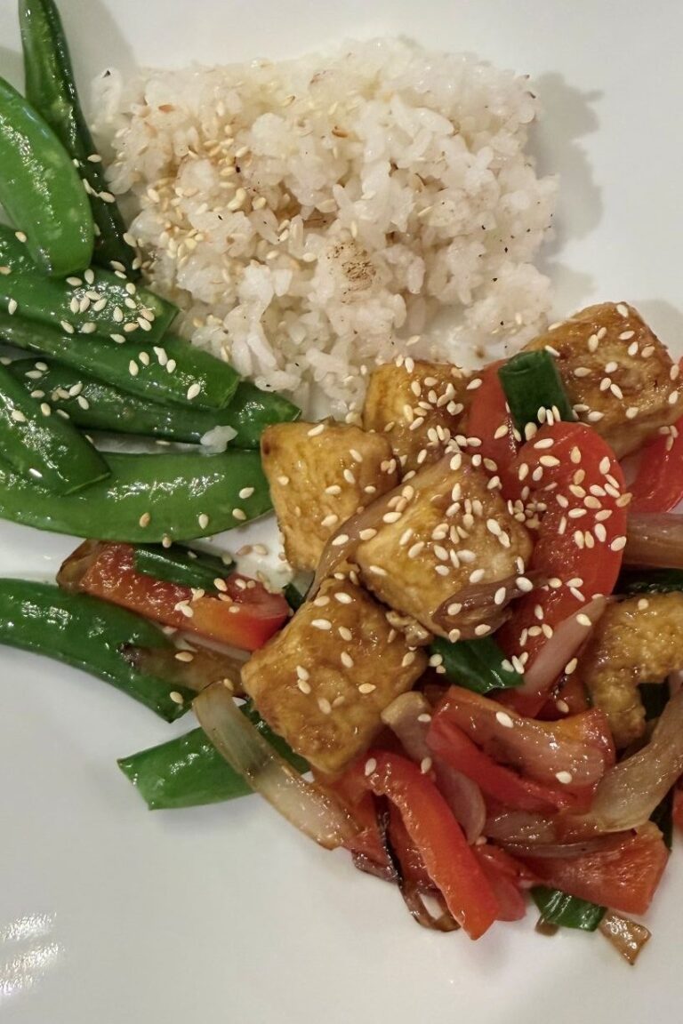 Tofu stir-fry with red bell peppers, sweet onions, and sesame seeds. Plated with sugar snap peas and rice.
