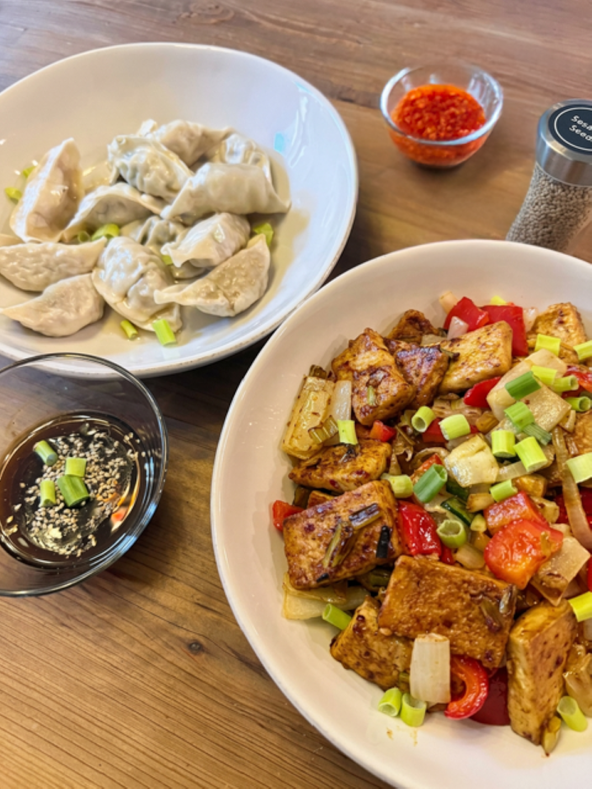 Spicy-sweet crispy tofu stir-fry with red bell peppers and sweet onions, topped with green onions and sesame seeds, served with dumplings, sweet chili sauce, and stir-fry sauce.
