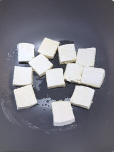 Instruction step 2 cooking the first side of tofu in a black wok. The side showing is un cooked.