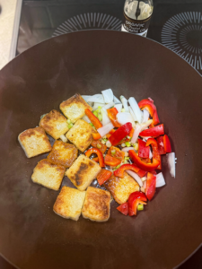 Crispy tofu cubes and sliced red bell pepper cooking in a skillet before adding sesame oil and aromatics