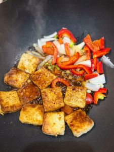 Spicy sweet sauce coating crispy tofu, red bell pepper, and green onions in a skillet