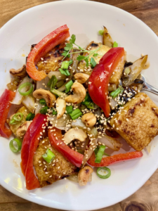 Spicy-sweet crispy tofu stir fry garnished with sesame seeds, cashews, and green onions